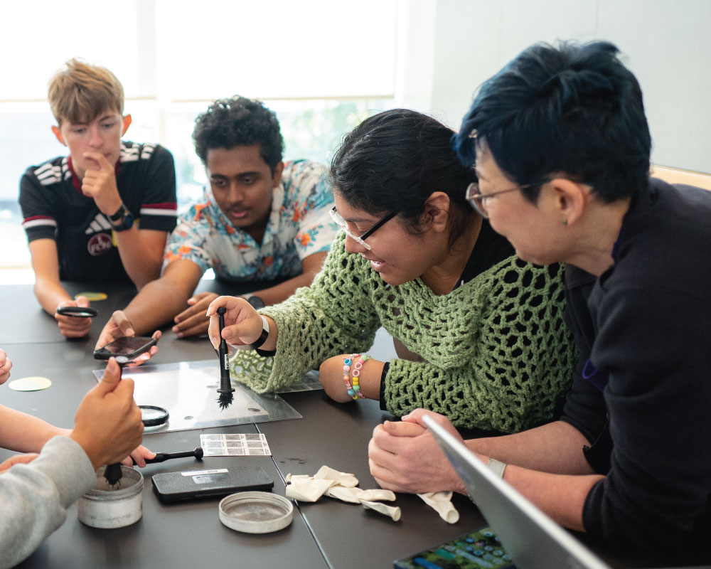 four students engaging in an forensics activity using fingerprint dust and brush